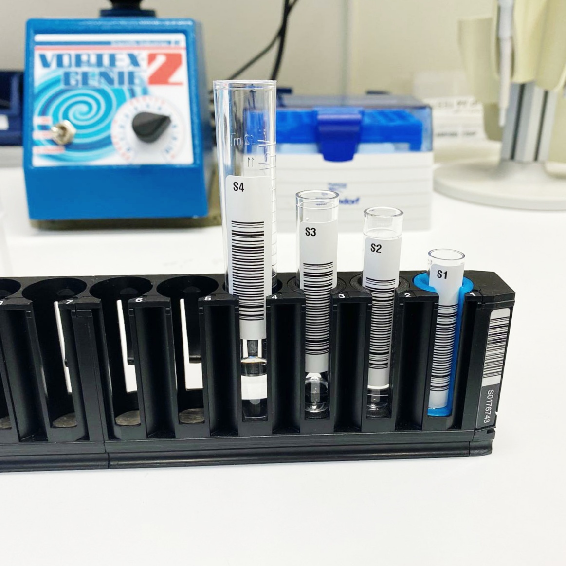Four sample tubes of different diameters standing in one Hamilton carrier, the narrowest seated in a blue 3D-printed adapter
