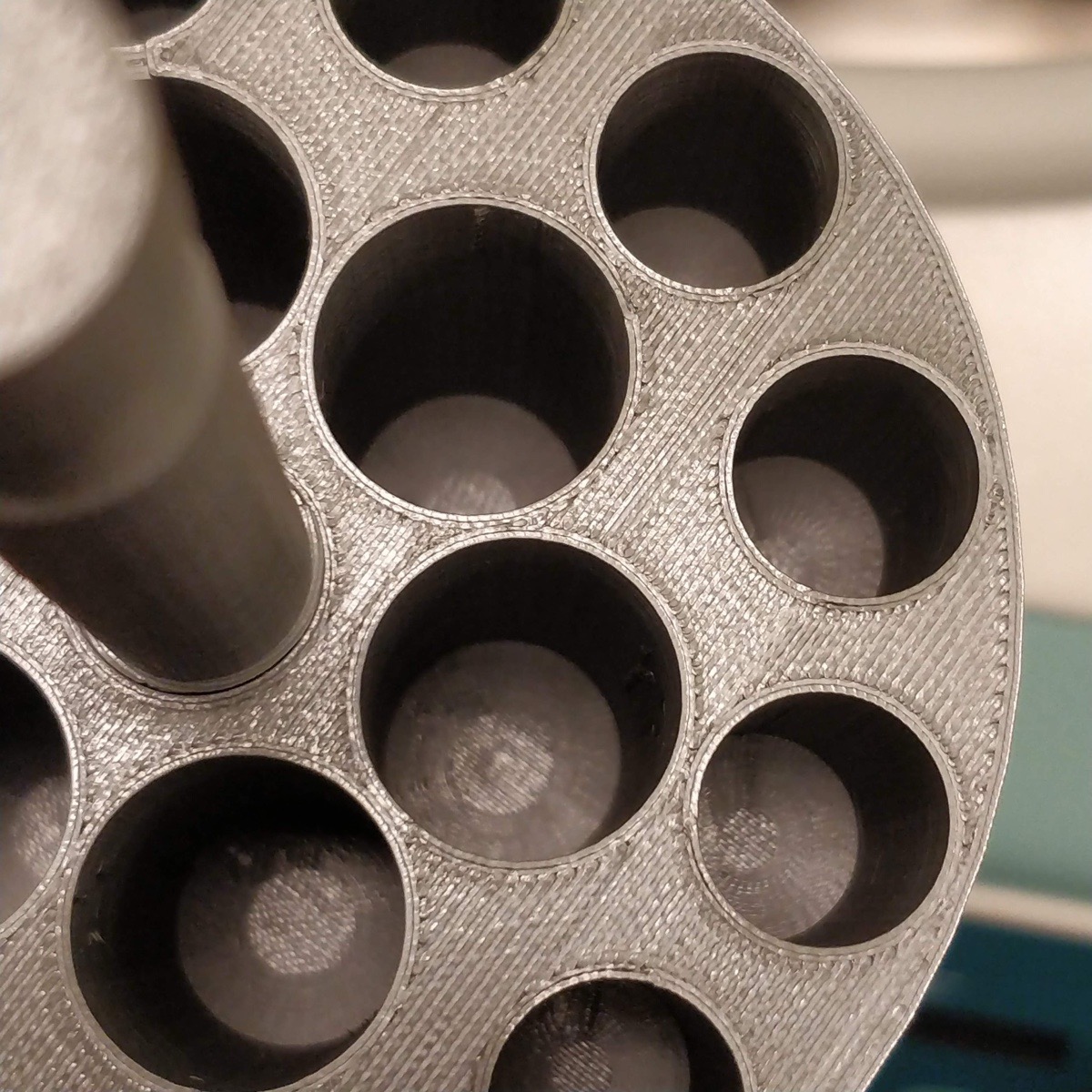 Close-up of a grey 3D-printed centrifuge insert, its print layers visible around wells of differing diameters, several of them stepped at the bottom